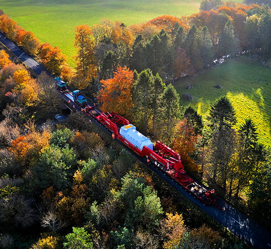 Girder frame transport travelling through a narrow road surrounded by trees